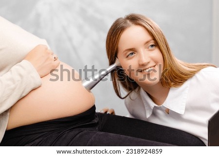 A gynecologist leans a stethoscope to a pregnant woman's belly and listens to the baby's heartbeat.