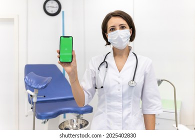  Gynecologist Shows An IPhone 12 With A Chromakey. The Doctor In The Gynecological Office Shows Mobile Phone With Green Mock Up Screen. Online Consultation With Doctor .June 16, 2021 - Moscow, Russia 