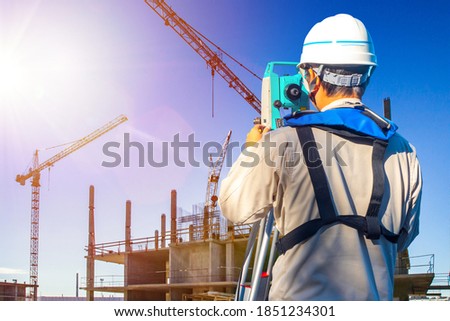 Gyodesist controls the work of builders. Builder with tachometer next to a construction site. Concept - codaster works. Concept - training for a surveyor. Man with a tachometer. Surveying Equipment.