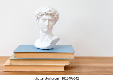 Gypsum Copy Of Head On A Bookshelf. Plaster Copy Bust Standing On Books. Ancient Greek Sculpture, Statue Of Hero On Wooden Table. Education Concept, Copyspace