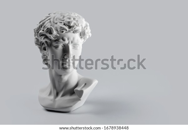 Gypsum statue of David\'s head.\
Michelangelo\'s David statue plaster copy on grey background with\
copyspace for text. Ancient greek sculpture, statue of\
hero