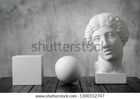 Gypsum white cube, sphere and head of an antique woman simple geometric shape on a gray fabric art background for learning to draw. Drapery and folds.