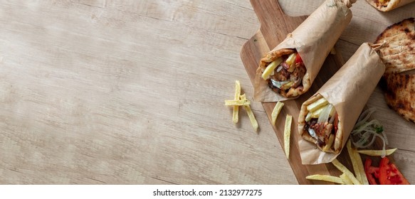 Gyro pita Shawarma preparation on wooden table, top view. Greek food, sliced meat, potato, tomato and tzatziki, paper wrap. Banner, Copy space