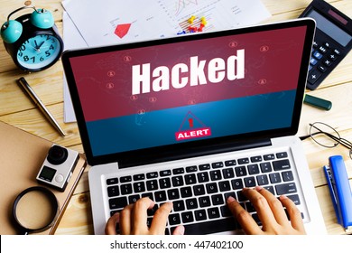 "Hacked" word on screen laptop display an alert when a man using it on wooden table with camera, clock, calculator and paper graph - hacking, alert and computer concept