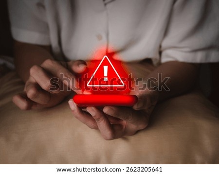 Hacker attack detection alert, sms fraud and scammer calls, fraudulent phone calls concept. Red triangle warning caution alert show on smart mobile phone in senior elderly hands, in the dark room.
