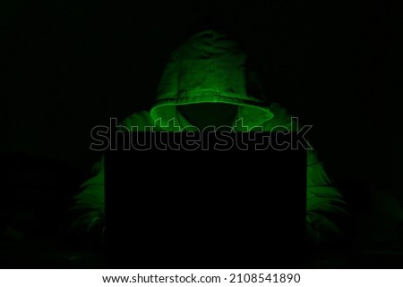 Hacker. Hacker attack. Developer. Software developer. Bandit. Criminal. Attack. information attack. Information. Cryptocurrency. Bitcoin. Computer. Green hacker. Darkness. Darknet. Masked man. Mask.