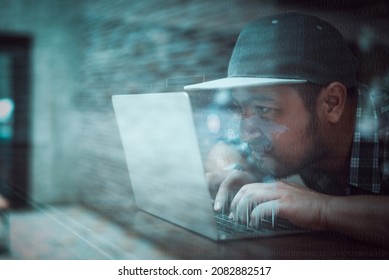 Hacker In Black Hoodie Using Laptop On The Desk To Hacking System With Binary Code And Upload The Malware With Virtual Screen Display Binary Code, Bar Graph And World Maps On The Background