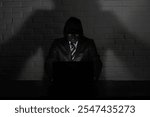 Hacker in black mask and hood at the table in front of the monitor
