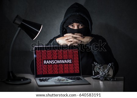 Hacker with computer screen showing ransomware attacking, alert in red digital binary background with hard disk drive lock. Cyber attack concept