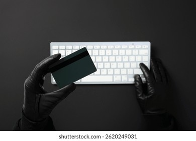 Hacker with credit card and keyboard committing cybercrime. Online payment fraud concept
