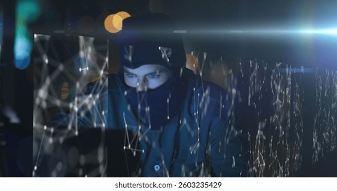 Hacker in dark room using laptop with digital network overlay, focused on screen. Cybersecurity, hacking, technology, espionage, coding, data