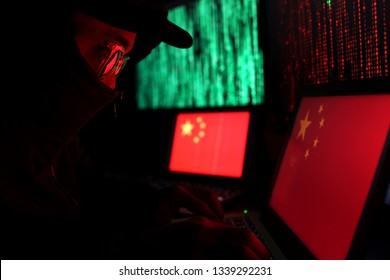 Hacker In A Dark Wearing Hoody And Cap Sitting In Front Of Computer With Digital China Flag Background And Binary Code, Cybersecurity Concept.