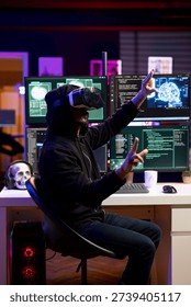 Hacker at desk coding on PC, using virtual reality to evade security with stealth malware. Evil man using VR headset and computer to hide malicious code from firewall detection systems