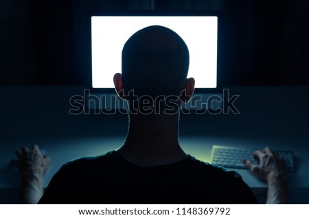 Hacker doing his crime on a desktop computer in the dark.