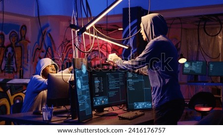 Hacker in hidden bunker uploading script on SSD that can launch DDoS attacks on any website, excited to show it to colleague. Cybercriminal happy after writing program that can crash servers