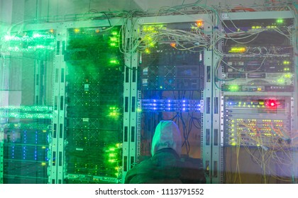 The hacker in the hood sits in the server room. The villain is behind the glass near the data center servers - Powered by Shutterstock