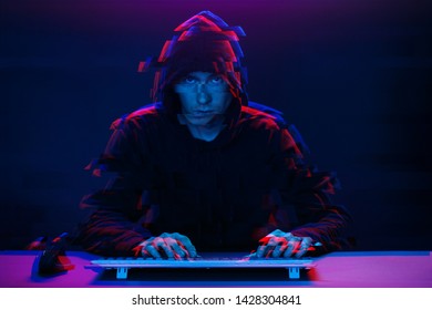 Hacker in the hood working with computer typing text in dark room. Image with glitch effect