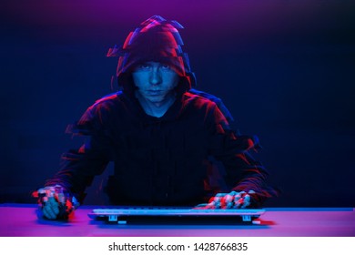 Hacker in the hood working with computer typing text in dark room. Image with glitch effect