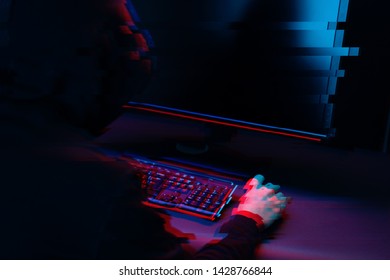 Hacker in the hood working with computer typing text in dark room. Image with glitch effect