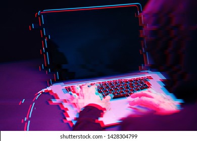 Hacker in the hood working with laptop typing text in dark room. Image with glitch effect