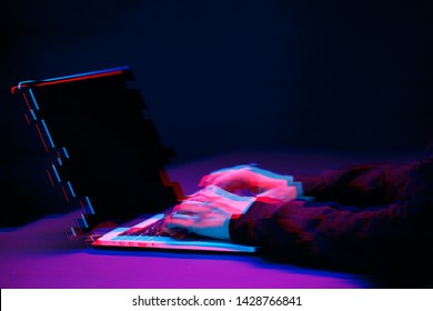 Hacker in the hood working with laptop typing text in dark room. Image with glitch effect