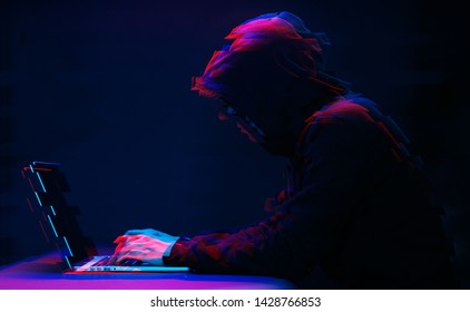 Hacker in the hood working with laptop typing text in dark room. Image with glitch effect