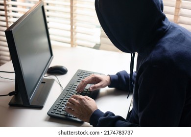 A Hacker In A Hooded Sweatshirt With A Hidden Face Typing On A Computer Keyboard.