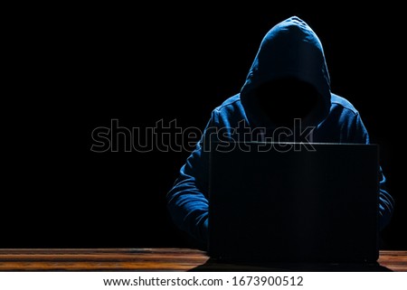 Hacker with laptop at the table breaks into the system