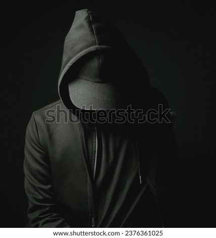 Hacker man black hat and hoodie sittingstanding in the dark looking down