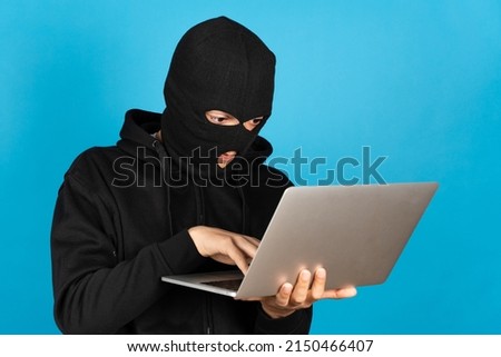 Hacker or online criminal typing on laptop isolated on blue background.