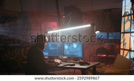 Hacker running phishing software on computer in criminals den with graffiti sprayed on walls. Cybercriminal doing malware programming in dark foggy underground base, breaching security