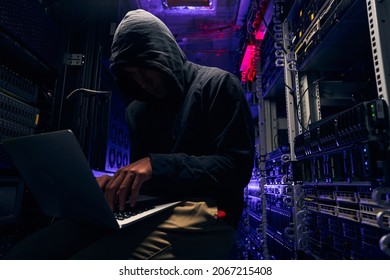 Hacker seated in server room launching cyberattack on laptop - Powered by Shutterstock