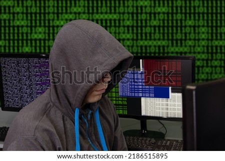 A hacker sits behind computer monitors on an abstract background, attacking and hacking servers with a virus. Creation and dissemination of disinformation, DDOS attack