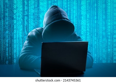 Hacker Using Computer laptop for Organizing Massive Data Breach Attack on Corporate Servers. Anonymous person in the hood sitting in front of computer working with laptop