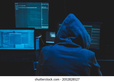 Hacker using computer for organizing massive data breach attack on goverment servers. Hacker in dark room surrounded computers