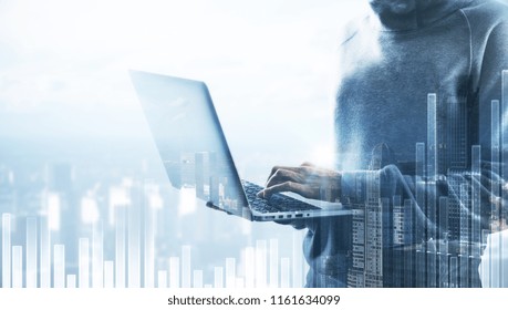Hacker using laptop on abstract city background with chart and copy space. Finance, hacking and communication concept. Double exposure 