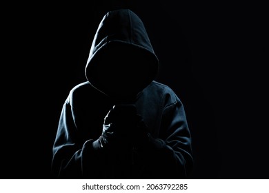 Hacker Using Smartphone. Men in black clothes with hidden face looks at smartphone screen on black background
