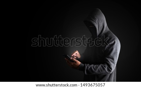 Hacker Using Smartphone. Men in black clothes with hidden face looks at smartphone screen on black background with copy space. with clipping path.