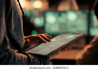 Hacker using spyware on digital tablet for illegal access on network, stealing passwords and cracking firewall encryption at night. Internet criminals hacking financial data, breaking into server.