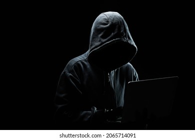Hacker without a face in a hood on with laptop in the dark.