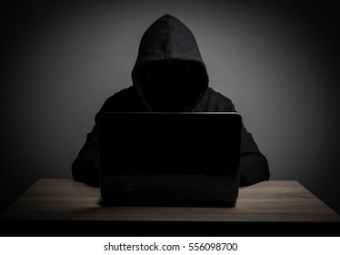 Hacker work front of his laptop computer with dark face.