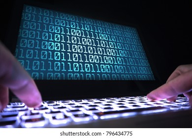 Hacker writing virus code with laptop in dark. Data crimimal in shadow. Cyber security, internet fraud and phishing concept. Close up of hands on keyboard and computer screen with binary numbers.