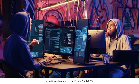 Hackers devising plan together, coding malware designed to exploit network backdoors, bypassing security measures such as logins and password protections in graffiti painted bunker.