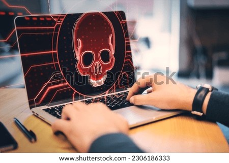 Hacking attack and online piracy creative concept with red skull digital hologram on modern laptop screen background and male hands on a keyboard, double exposure
