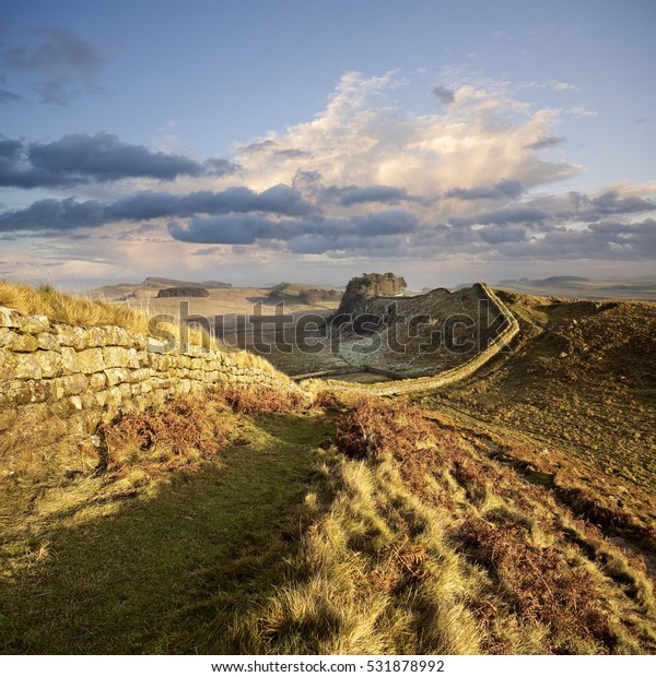 Hadrian\'s\
Wall snakes its way across the landscape in Northumberland,\
England, illuminated by a pastel winter\
sunset