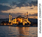 The Hagia Sophia from the Bosphorus Strait, Istanbul, glowing in golden hues at twilight with reflections in the water.