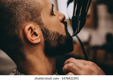 Hair beard and mustache treatment in barber shop. Young, bearded, muscular,  handsome barber making haircut of attractive bearded man in barbershop