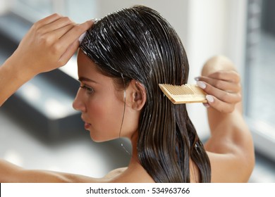 Hair Beauty. Closeup Of Beautiful Woman Hairbrushing With Comb And Using Conditioner. Young Female Model Putting Refreshing Mask On Long Wet Hair With Wooden Comb. Health Care. High Resolution 