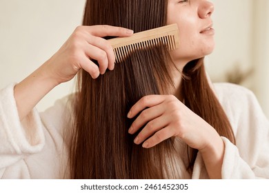 Hair care, beauty and woman combing her hair with a wooden comb while taking care of herself. - Powered by Shutterstock