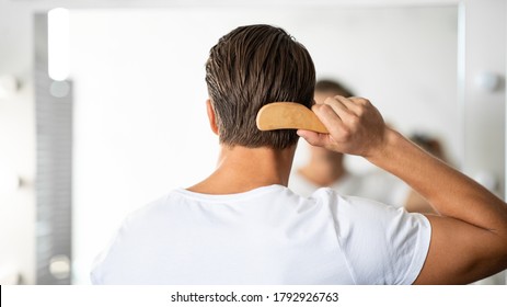 Hair Care. Close up rear view of young man hairbrushing with comb, looking in mirror